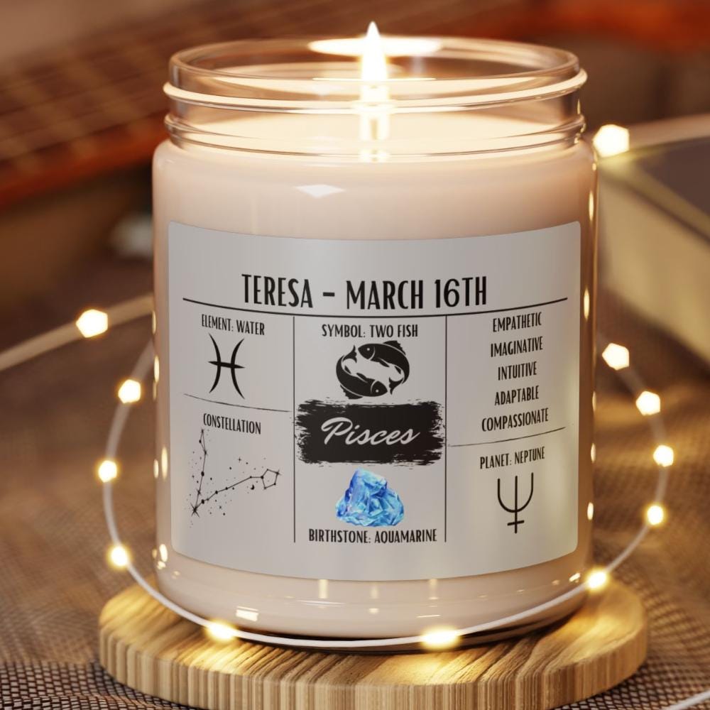 A personalized Pisces zodiac candle with a label showing the Pisces constellation, birth date, and name. The candle is set in a jar with a wooden lid, presented on a wooden platform with small LED lights around it.